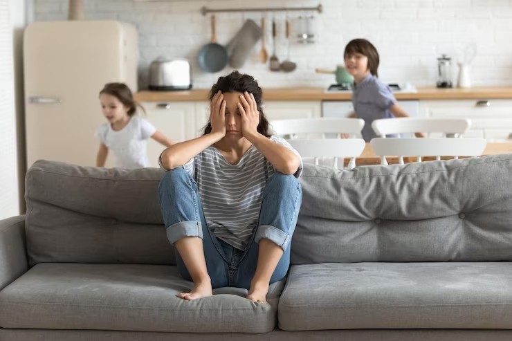 A tired mum resting on the couch, surrounded by active kids.